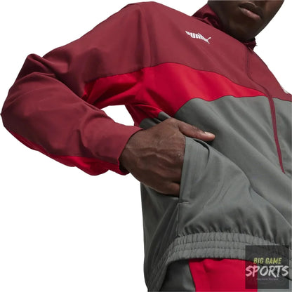 A close-up of a person wearing a Puma windbreaker jacket in a colorblock design of dark red, bright red, and gray. The model is shown from the chest down, with one hand in the pocket of the jacket.