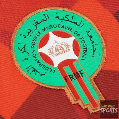 Close-up of an embroidered Morocco national football team crest patch on a red and orange striped fabric background.