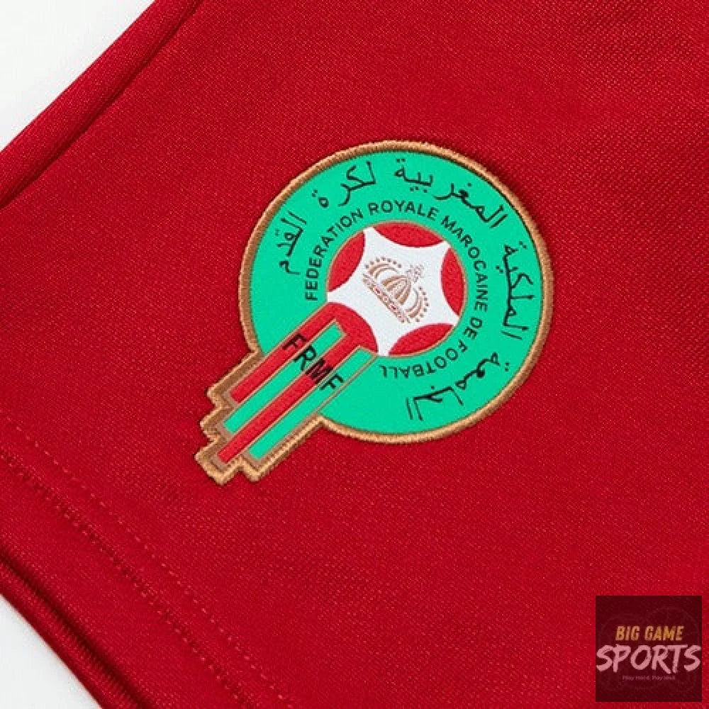 A close-up of a red fabric garment featuring an embroidered circular Morocco football crest in green, red, white, and gold with Arabic text.