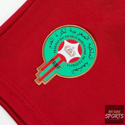 A close-up of a red fabric garment featuring an embroidered circular Morocco football crest in green, red, white, and gold with Arabic text.