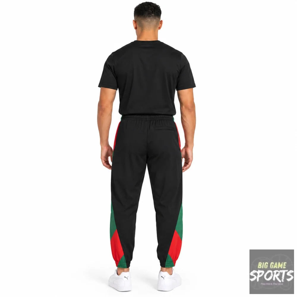 A man viewed from the back wearing black jogger-style track pants with red and green side panels and white sneakers, against a plain white studio background.