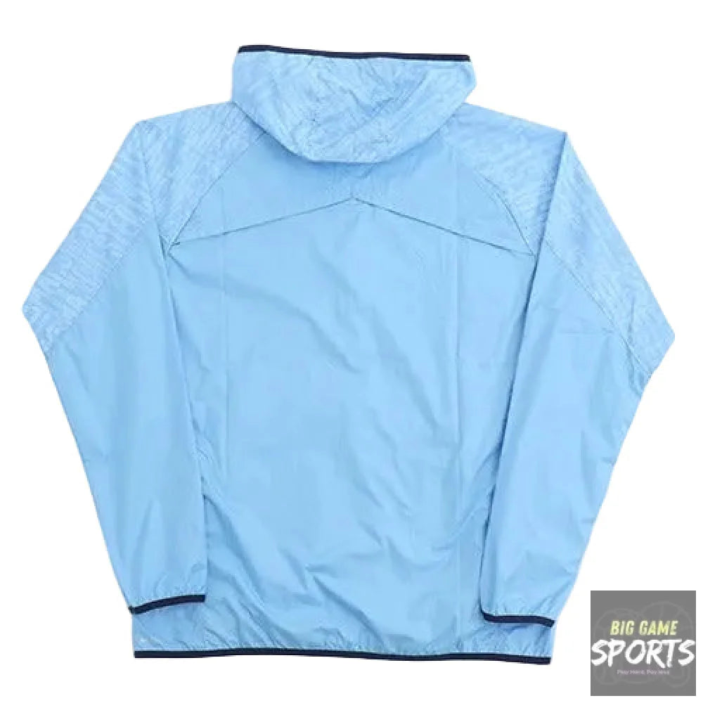 A light blue hooded windbreaker jacket shown from the back, laid flat on a white background. The jacket features subtle tonal patterning on the sleeves and hood, with contrasting dark navy piping along the collar, cuffs, and hem.