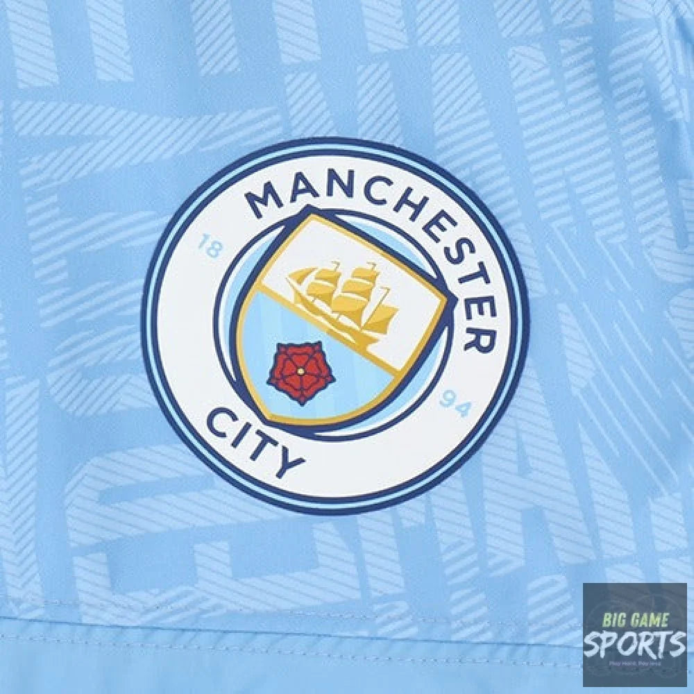 Close-up of a Manchester City soccer jersey in light blue, featuring the club's circular crest on the chest.