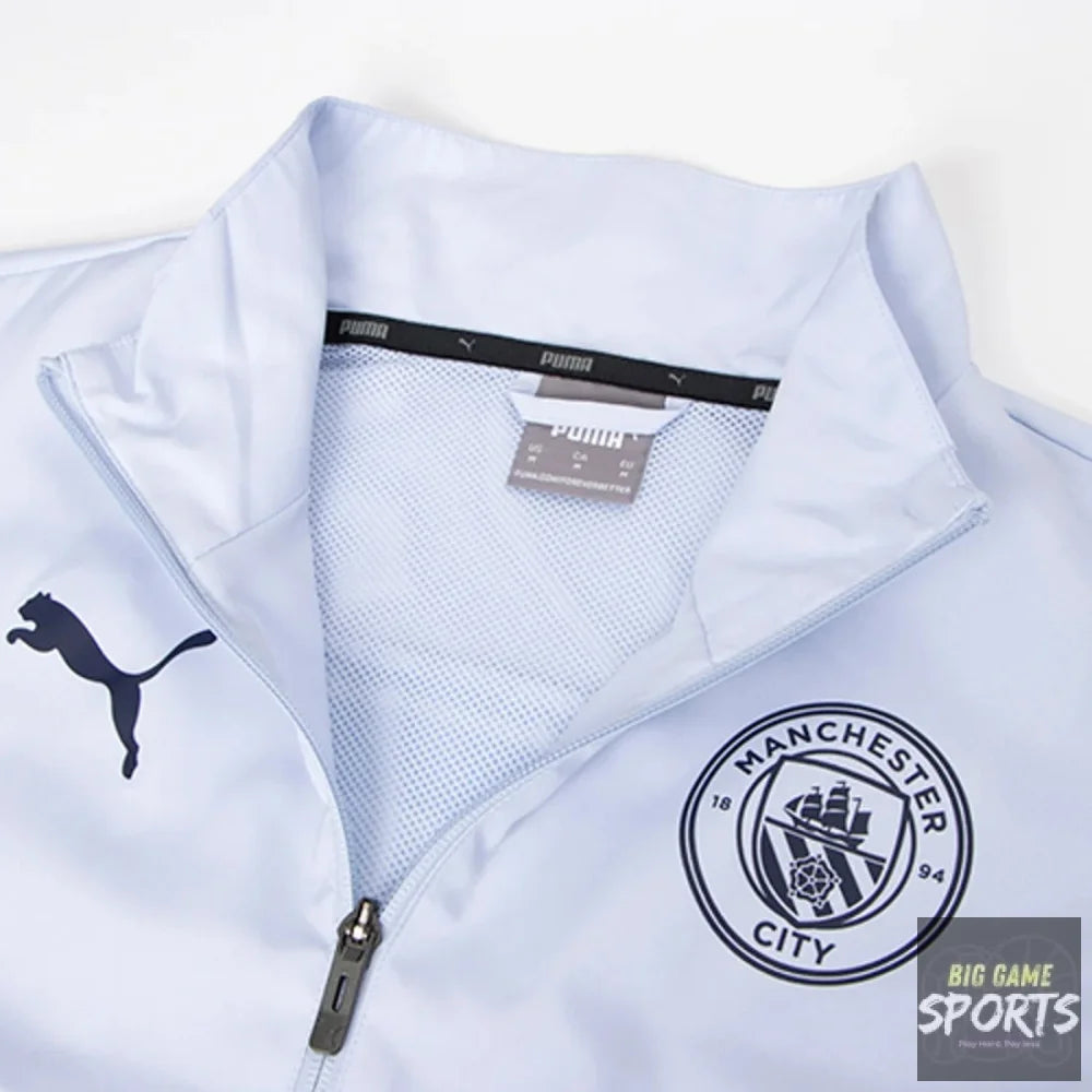 A close-up of a light blue Puma zip-up jacket featuring the Manchester City crest on the left chest and the black Puma cat logo on the right chest.