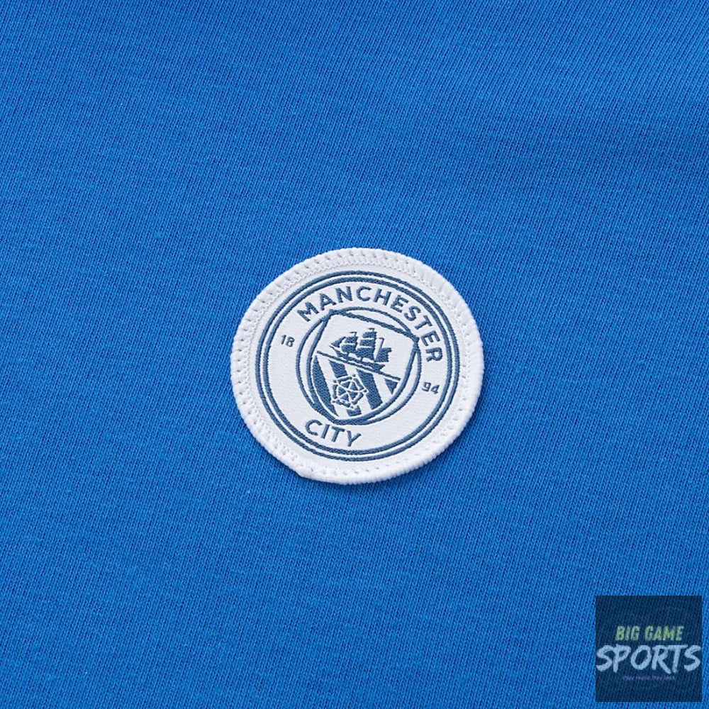 A close-up of a Manchester City FC embroidered crest patch on a vibrant blue knit fabric background.