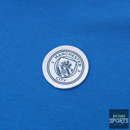 A close-up of a Manchester City FC embroidered crest patch on a vibrant blue knit fabric background.