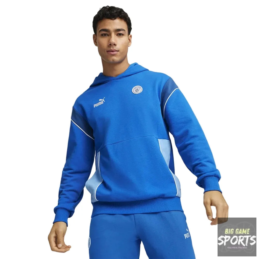 A male model wearing a bright blue Puma tracksuit with white and light blue accents, featuring a pullover hoodie and matching sweatpants, set against a neutral gray studio background.