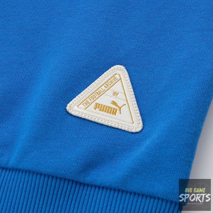 A close-up of a bright blue ribbed knit garment featuring a triangular embroidered Puma patch with 'The Football League' text.