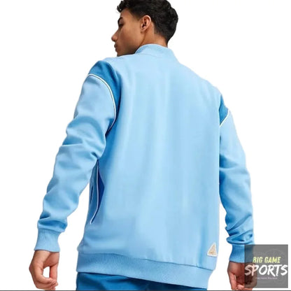 A man wearing a light blue track jacket, shown from the back, in a studio setting with a light gray background.