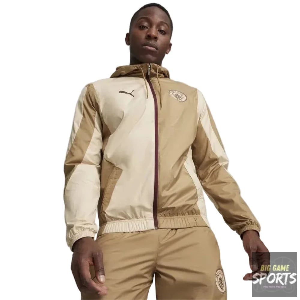A man wearing a beige and cream color-blocked Puma windbreaker jacket with a matching pair of beige trousers, standing against a light gray studio background.