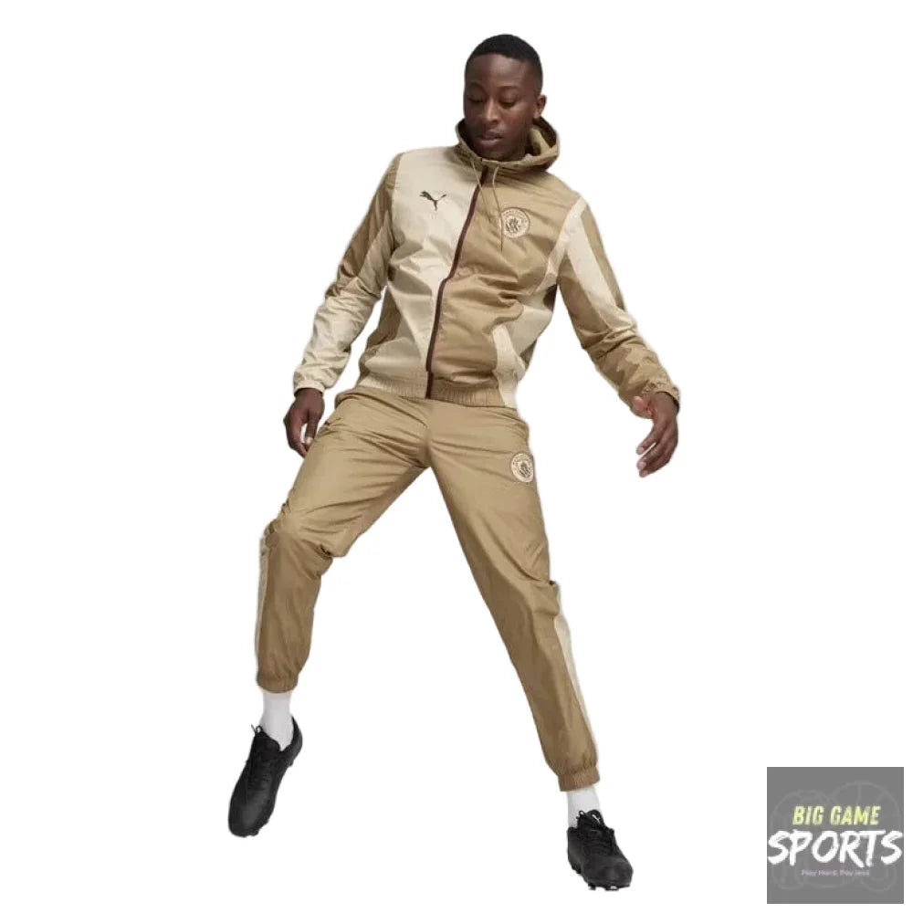 A model wearing a beige and cream Puma tracksuit with a hooded jacket and matching joggers, balancing a soccer ball on the floor in a studio setting.