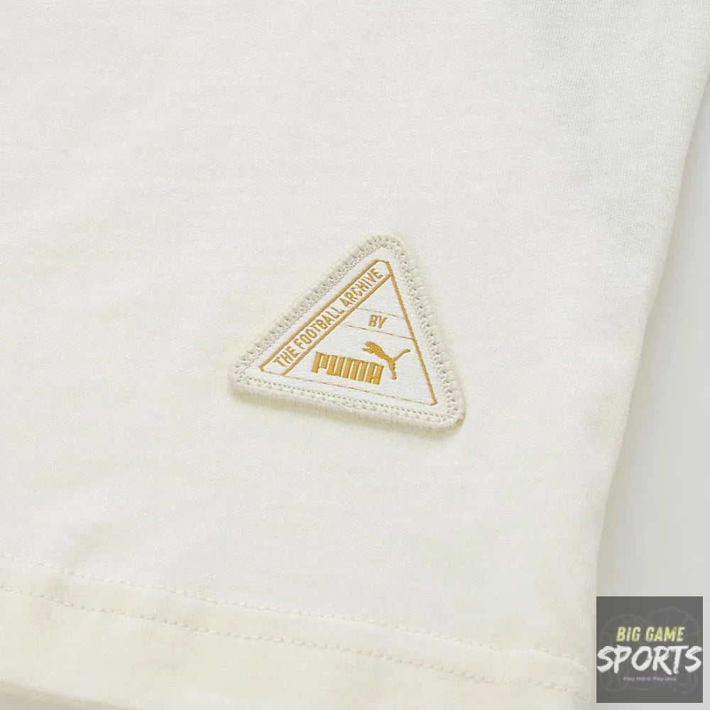 Close-up of a white Puma garment featuring a triangular embroidered logo patch in gold and off-white on the fabric.