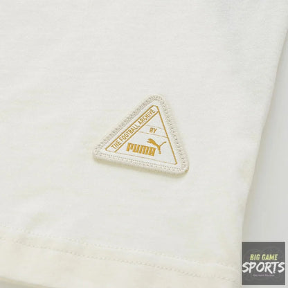 Close-up of a white Puma garment featuring a triangular embroidered logo patch in gold and off-white on the fabric.