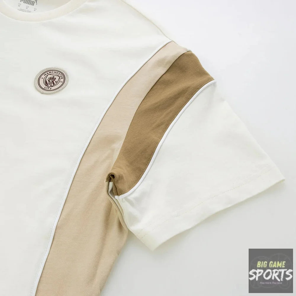 A close-up of a short-sleeve t-shirt showing a color-blocked design with a white body, a beige vertical stripe, and a tan sleeve panel. A circular embroidered patch is visible on the chest.