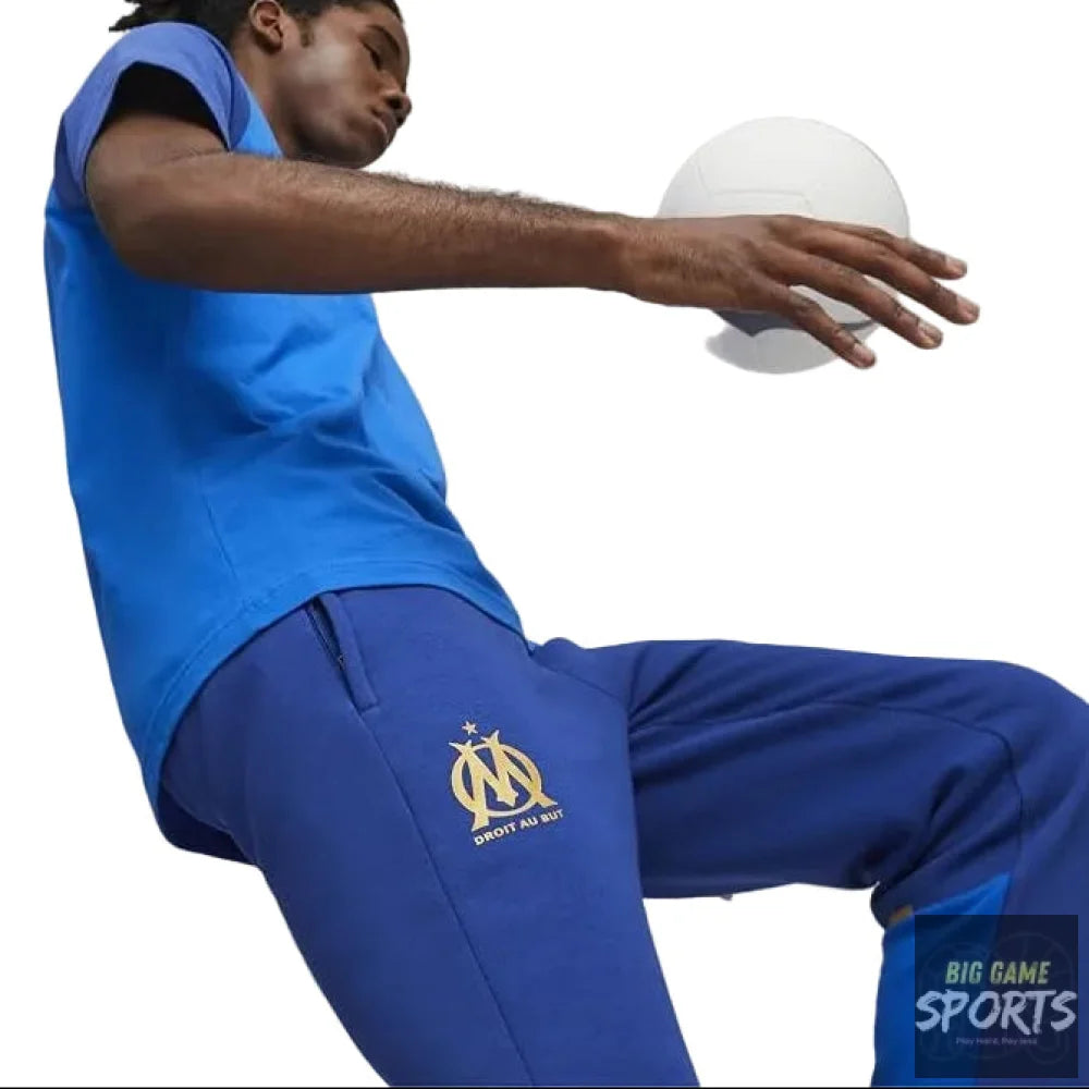 Person wearing blue sports outfit with a logo, holding a ball in a gym setting