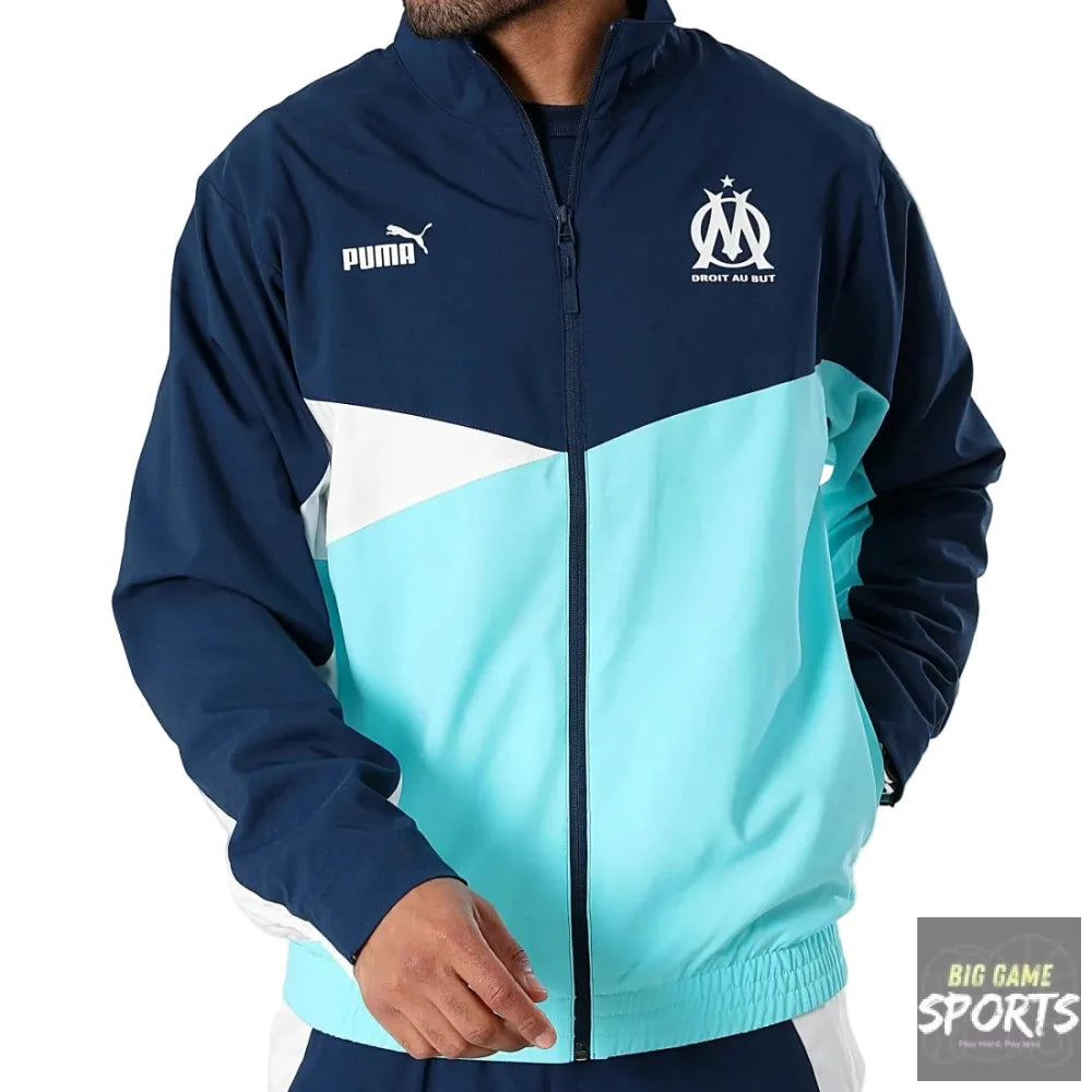 A man wearing a Puma Olympique de Marseille colorblock jacket in navy blue, light blue, and white, featuring the club's crest on the left chest and the Puma logo on the right.