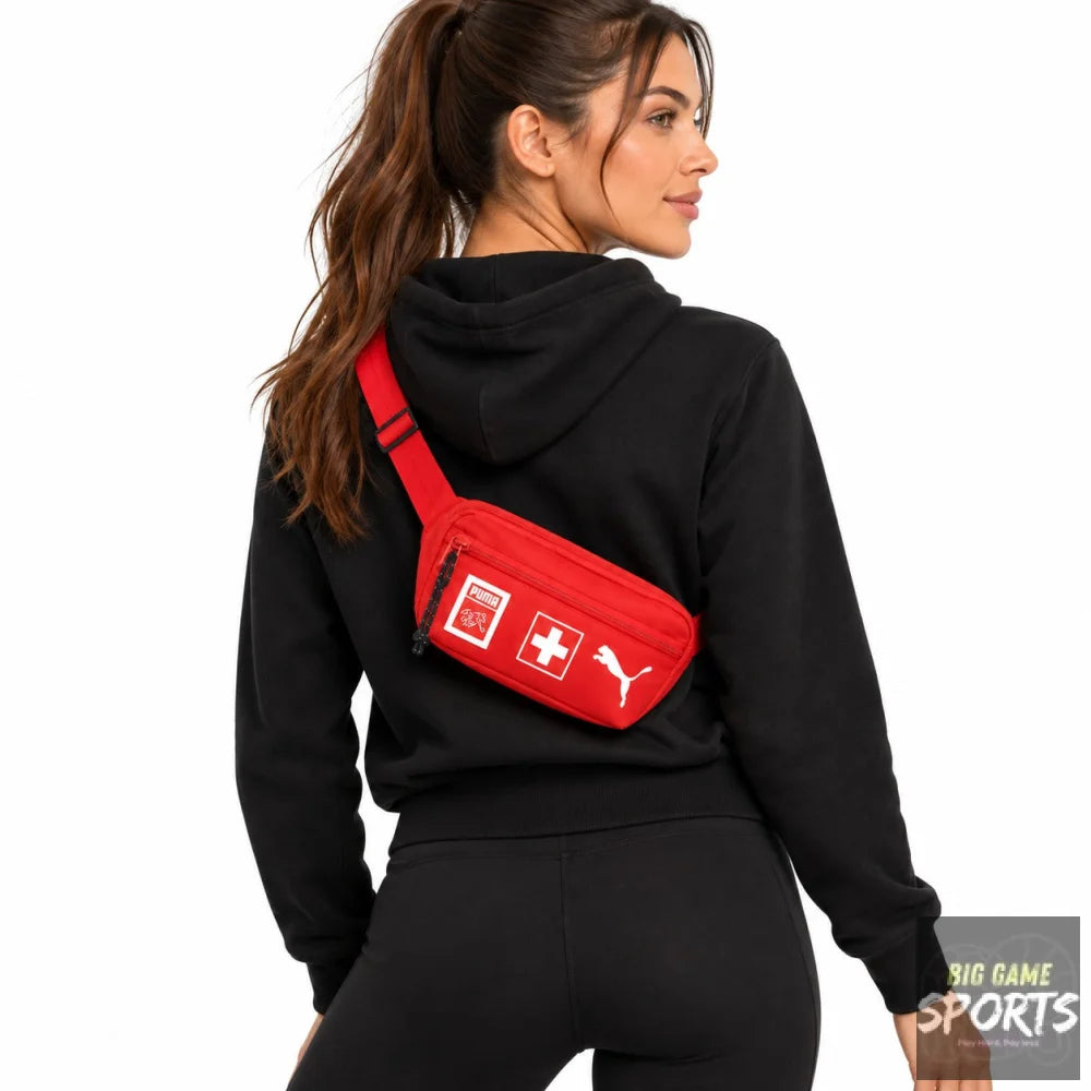A woman wearing a black hoodie and black leggings from the back, wearing a red Puma crossbody bag with Swiss flag graphics on the front, against a solid white background.