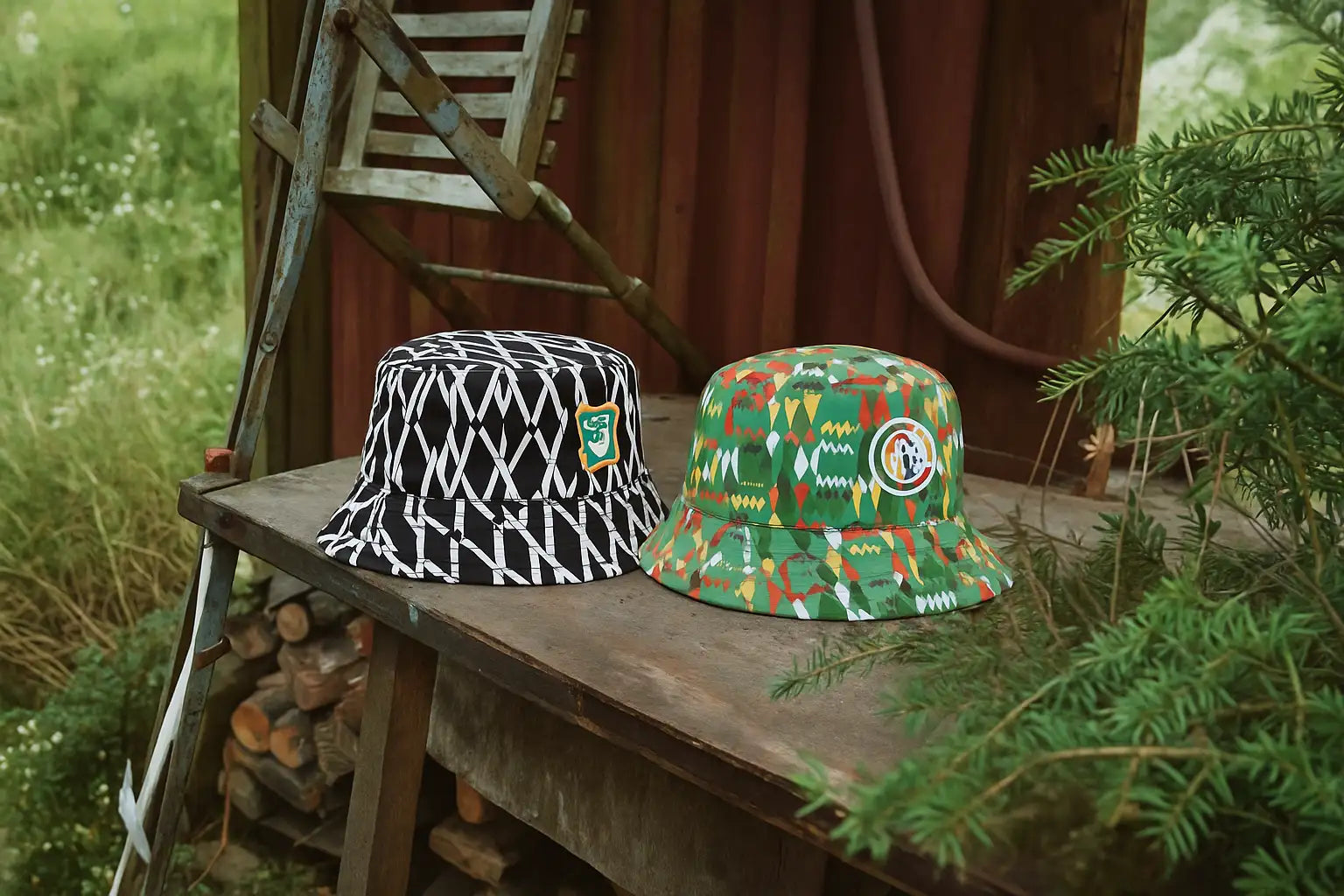 Two bucket hats, one in black and white geometric pattern with a green emblem patch, the other in vibrant multicolored tribal-inspired print featuring an embroidered circular logo.